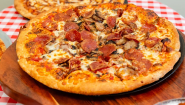 Close-up of a pepperoni and sausage pizza with melted cheese on a wooden serving tray.