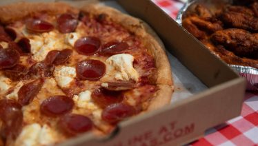 Pepperoni pizza and wings from Manny and Olga's on a red checkered tablecloth.