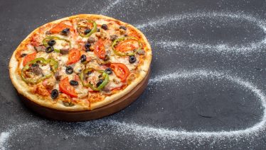 Cheese pizza on wooden board with olives and pepperoni, flour swirls forming a galaxy pattern around it.
