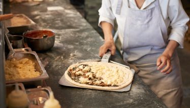 A person in an apron preparing pizza at a floured counter, like at Manny & Olga’s kitchen.