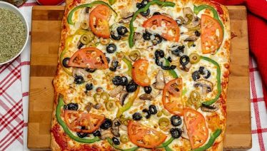 Square meat pizza with fresh tomato slices and sides from Manny & Olga’s, showcasing local flavor in Washington, DC.