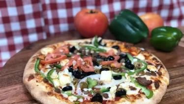 Freshly baked pizza at Manny & Olga’s topped with locally sourced tomatoes, green peppers, olives, and melted cheese.